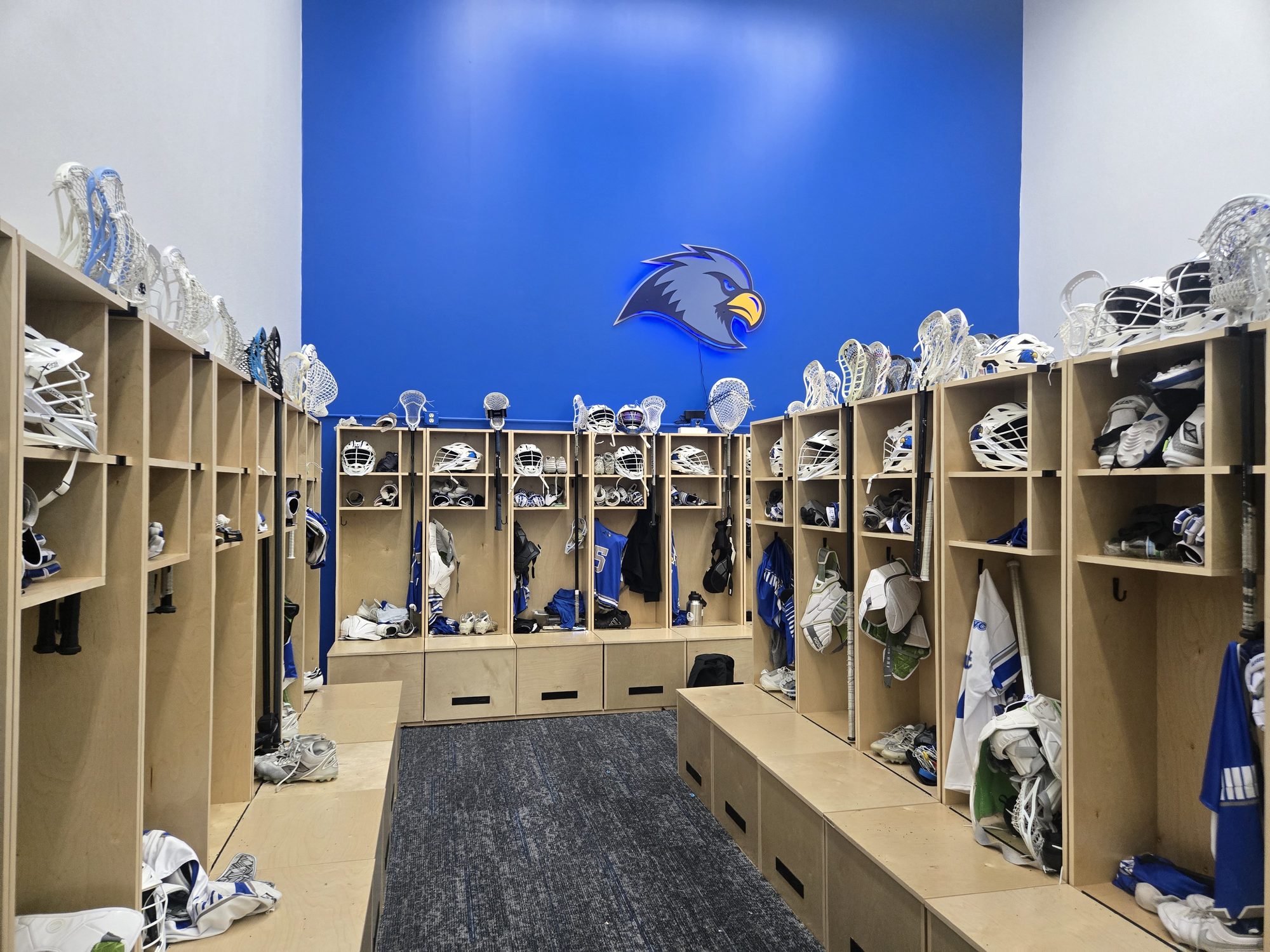 Rockhurst University lacrosse locker room lined with birch lockers holding helmets, sticks and gear