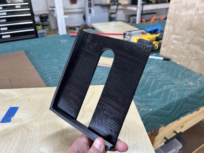 3D-printed black stick-slot insert held over a plywood top panel