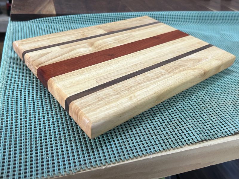 Maple cutting board with a red padauk stripe and two walnut stripes